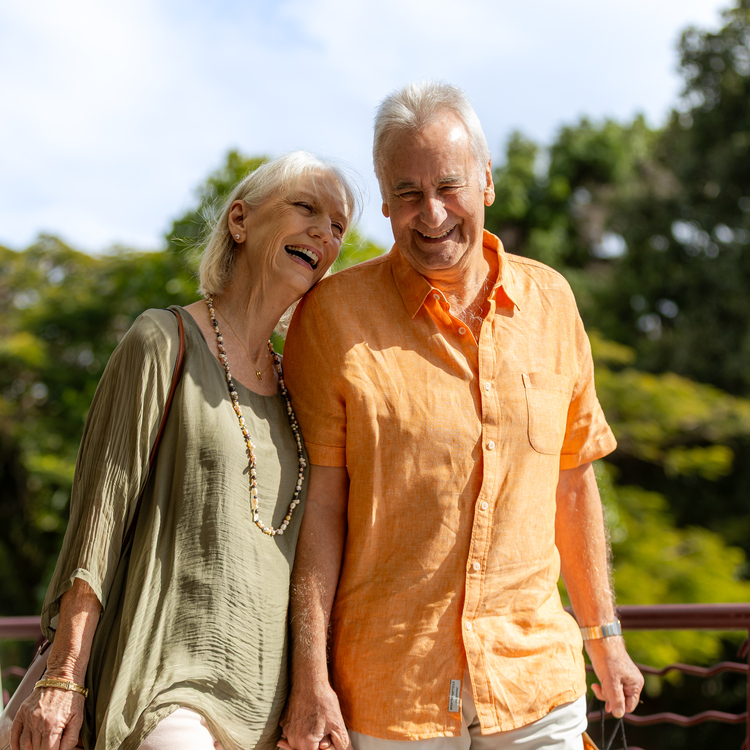 An elderly couple smiling and walking along a retirement village in colourful linen clothing