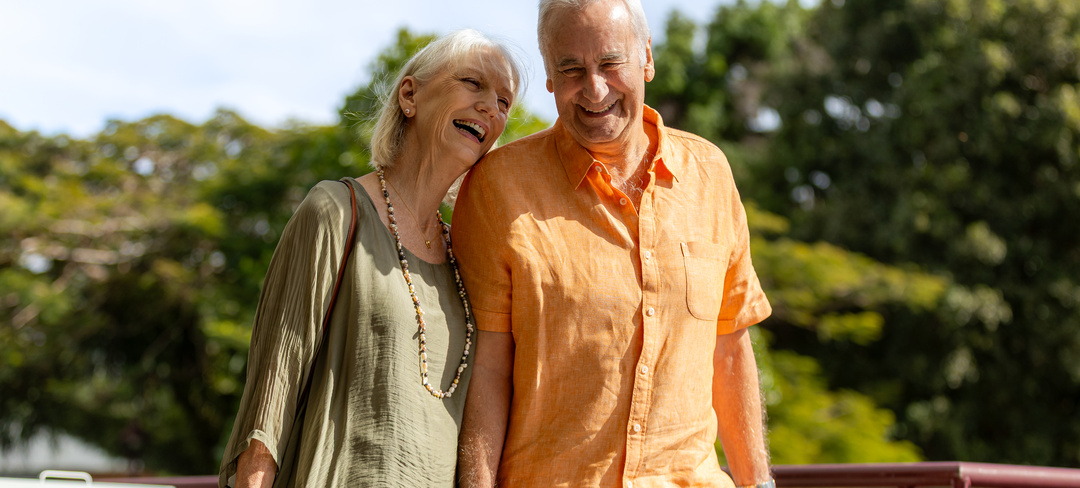 An elderly couple smiling and walking along a retirement village in colourful linen clothing
