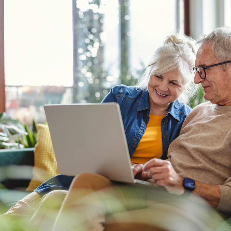 Senior couple using laptop while sitting on sofa in living room at home