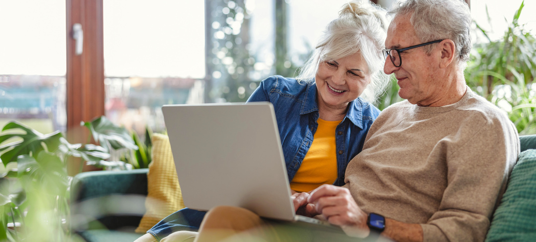 Senior couple using laptop while sitting on sofa in living room at home