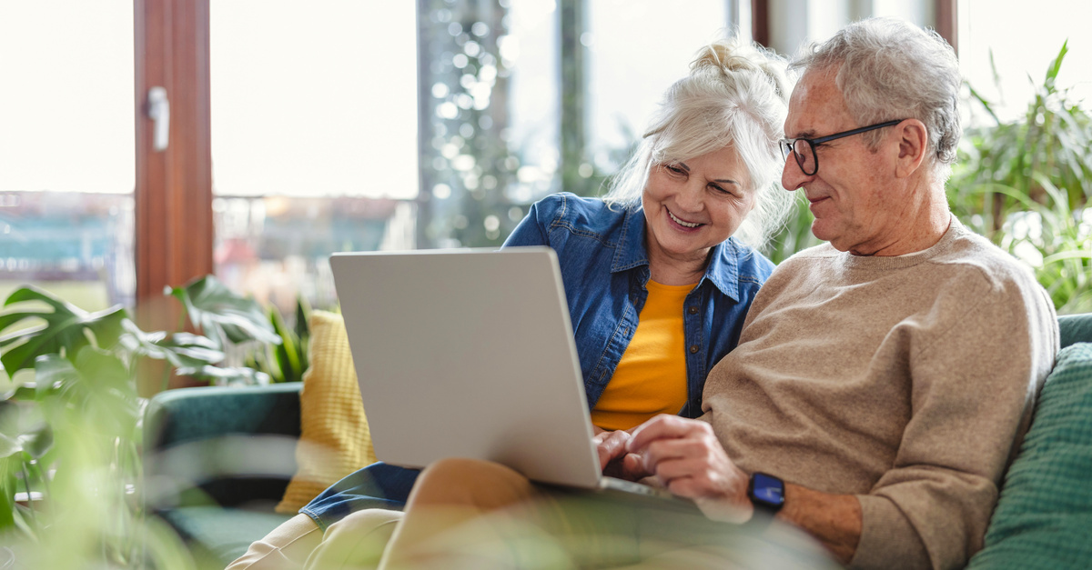Senior couple using laptop while sitting on sofa in living room at home