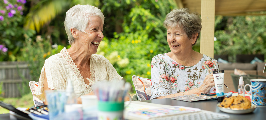 Two female residents of Hibiscus Buderim Meadows retirement village sitting at a table and painting together
