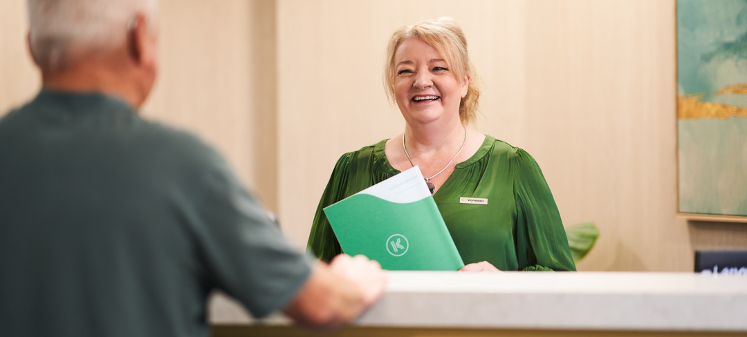 A female Keton employee smiling at a resident at a village reception holding a green Keyton binder