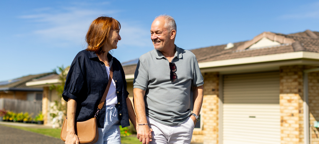 A retired couple holding hands and walking through a retirement village