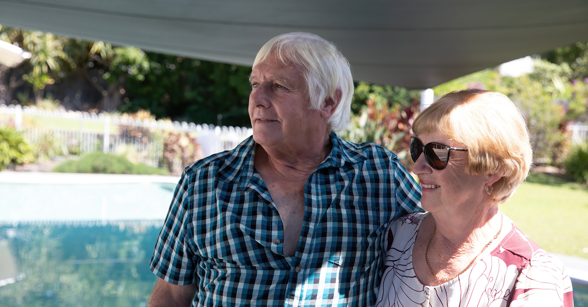 Older man and woman arm in arm while standing next to a pool