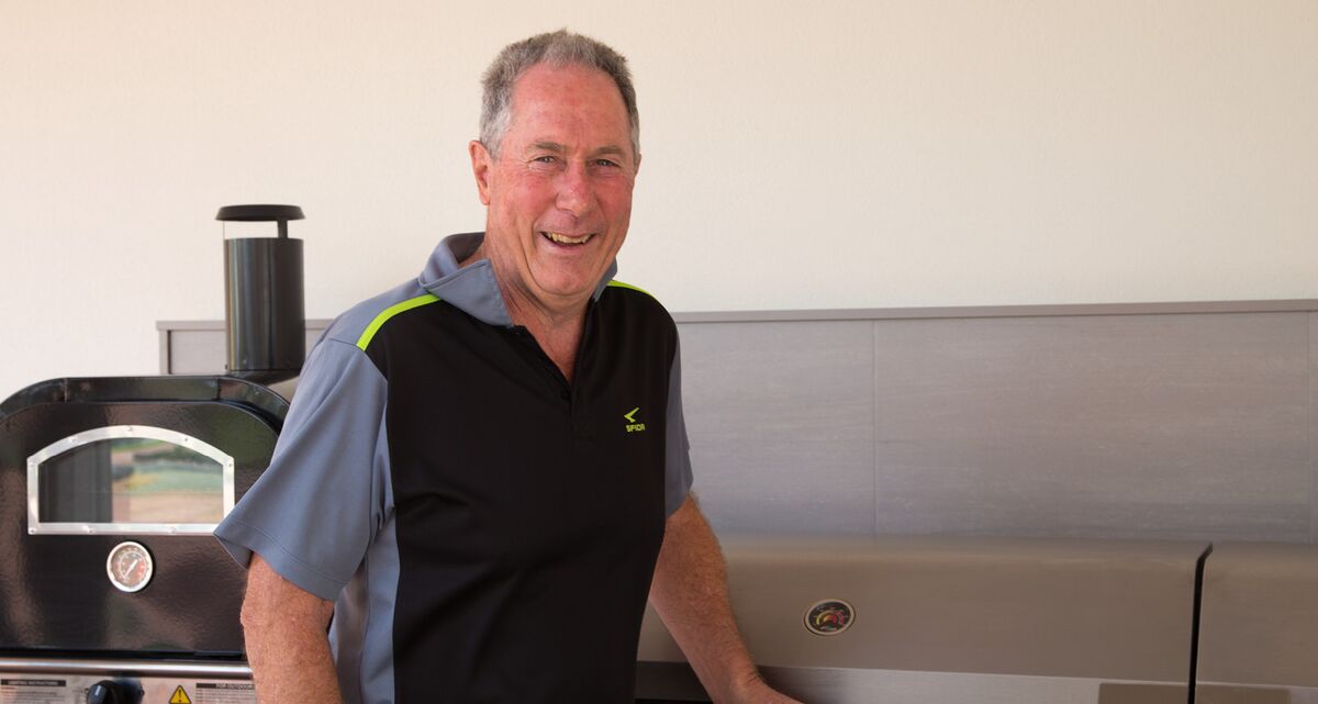 Retirement village resident Alan Gulliver wears a black and grey sports polo and smiles as he looks at the camera.
