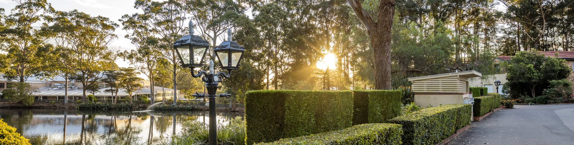 A scenic pathway in Brentwood Village next to a lake, bordered by a neatly manicured green English Box hedge.
