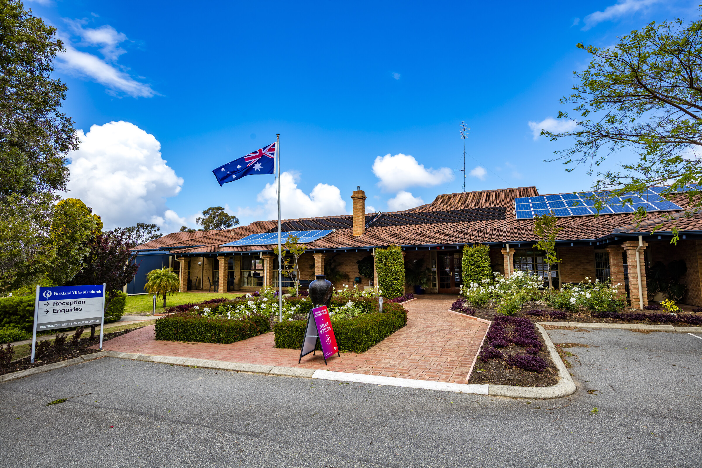 Parkland Villas Mandurah main entrance outside with landscaped garden, road and flag pole, solar panels on roof
