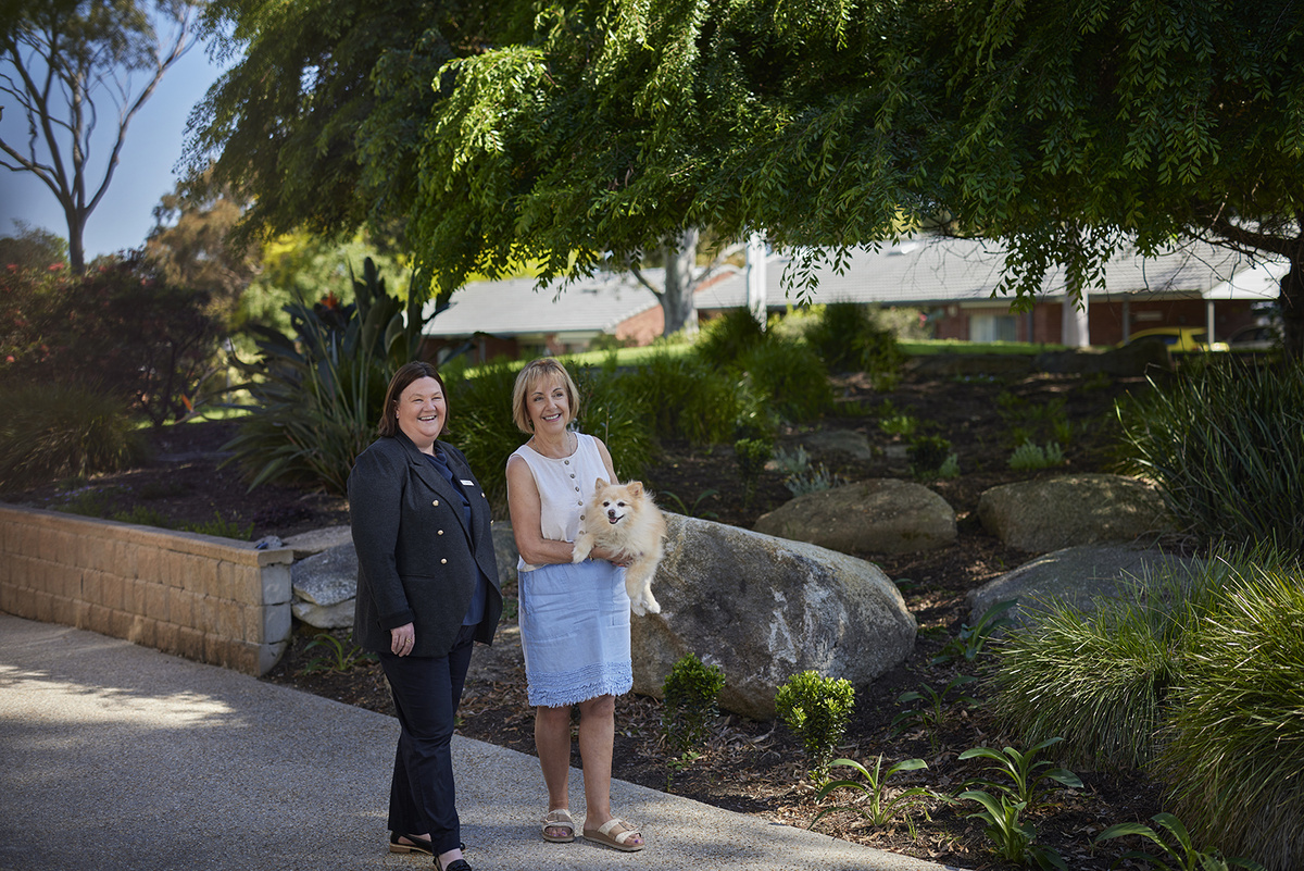 A resident and a staff member are walking in the village premises with a dog