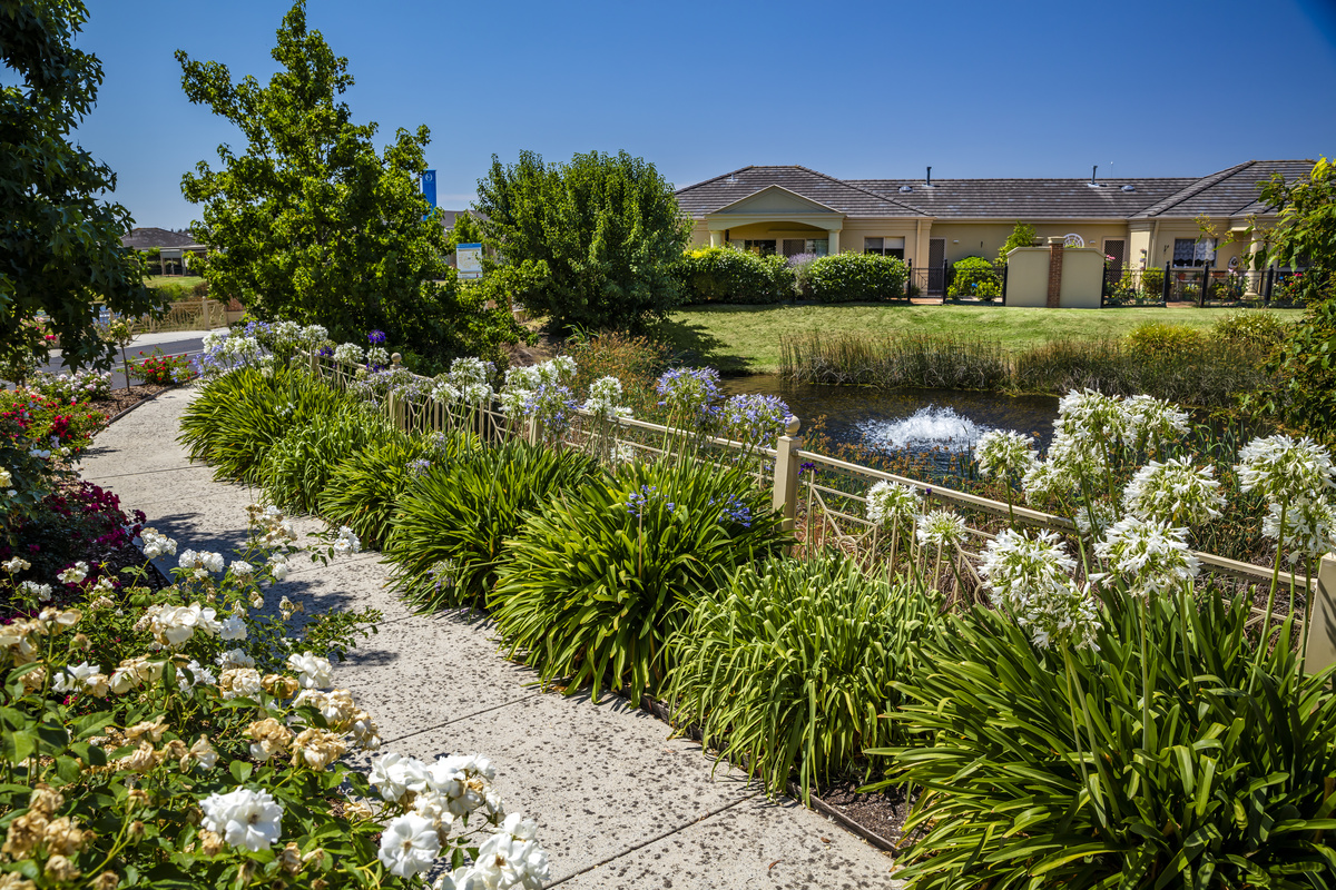 Waterford Valley Lakes image of path through garden next to pond with water feature, homes in the background