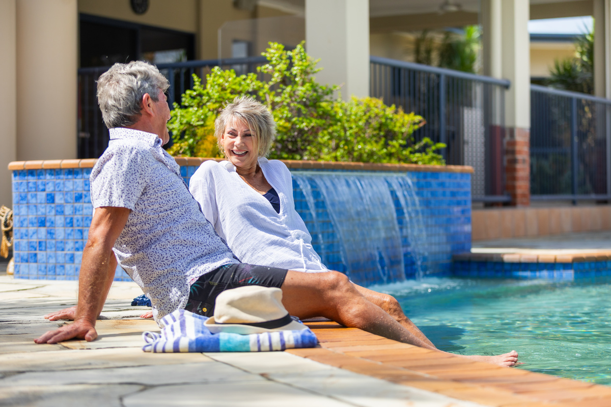 A senior couple sitting by the pool and smiling at each other