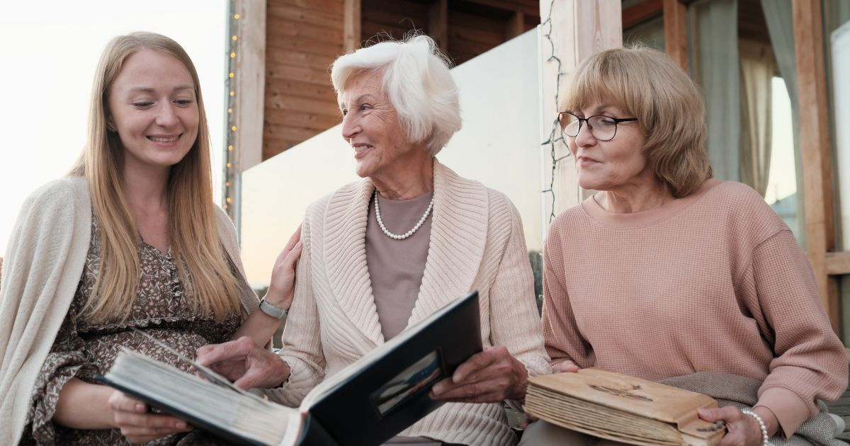  A senior woman looking through a family album with two young women
