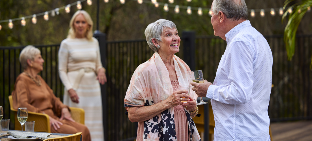 A group of retirement village residents gathered outside on a patio with fairy lights in the back having a chat