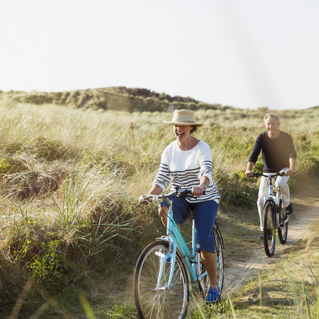 An elderly couple riding their bikes along the dunes at the beach
