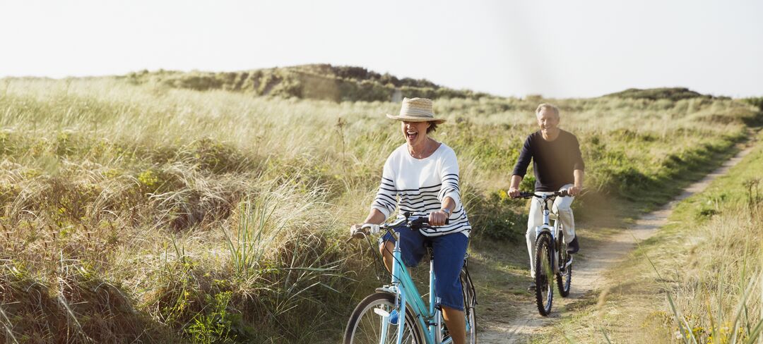 An elderly couple riding their bikes along the dunes at the beach