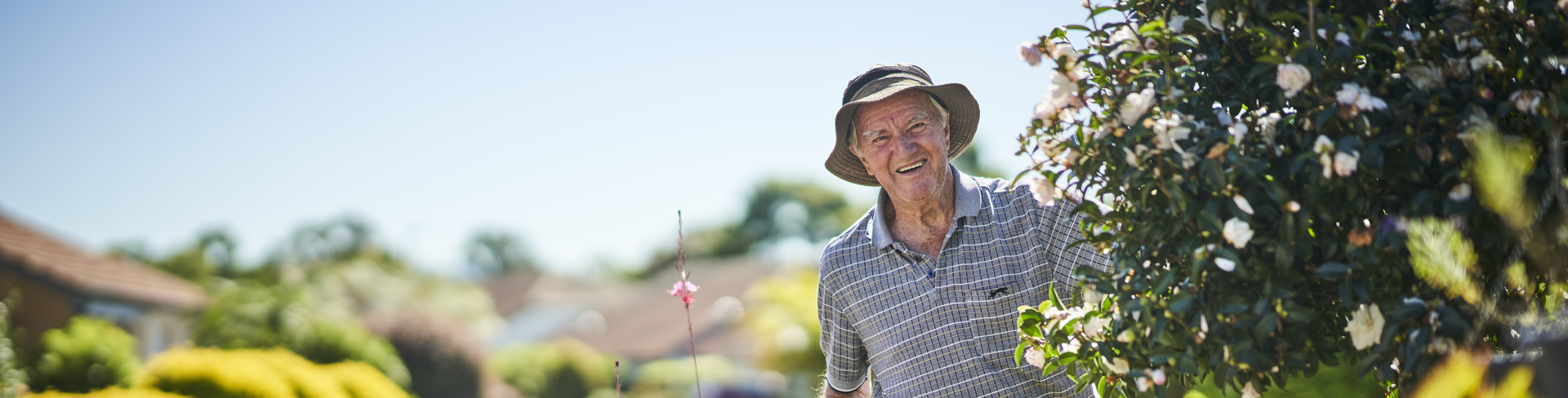 An elderly man wearing a hat standing in his garden in a retirement village