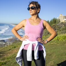 A woman in a pink singlet and black workout leggings stands with hands on hips, ready to work out with our exercise tips for seniors.