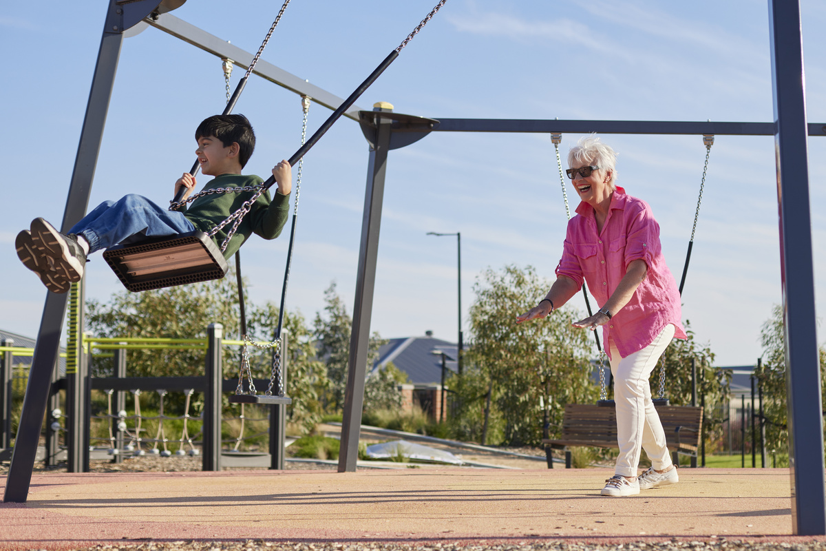 A grandmother is pushing her grandchild on the swing at the playground.