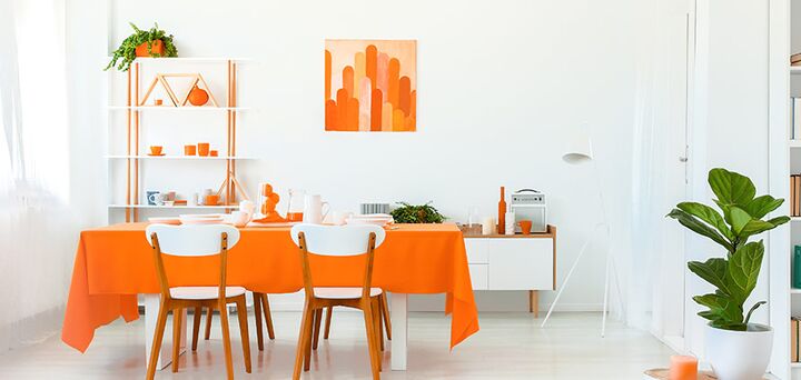 A dining room with white walls, white and timber furniture and orange decor and accents.