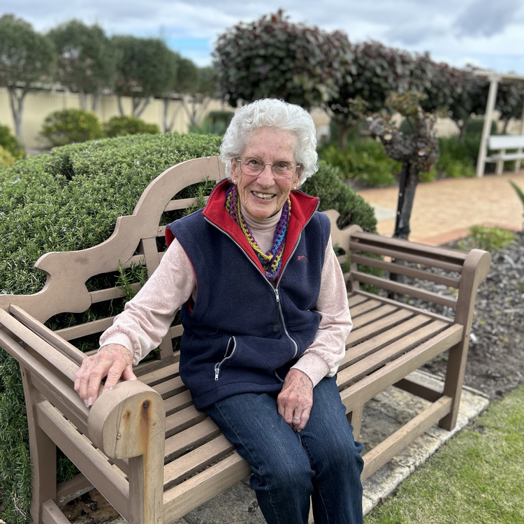 an old woman looking and smiling at the camera sitting on the bench outside