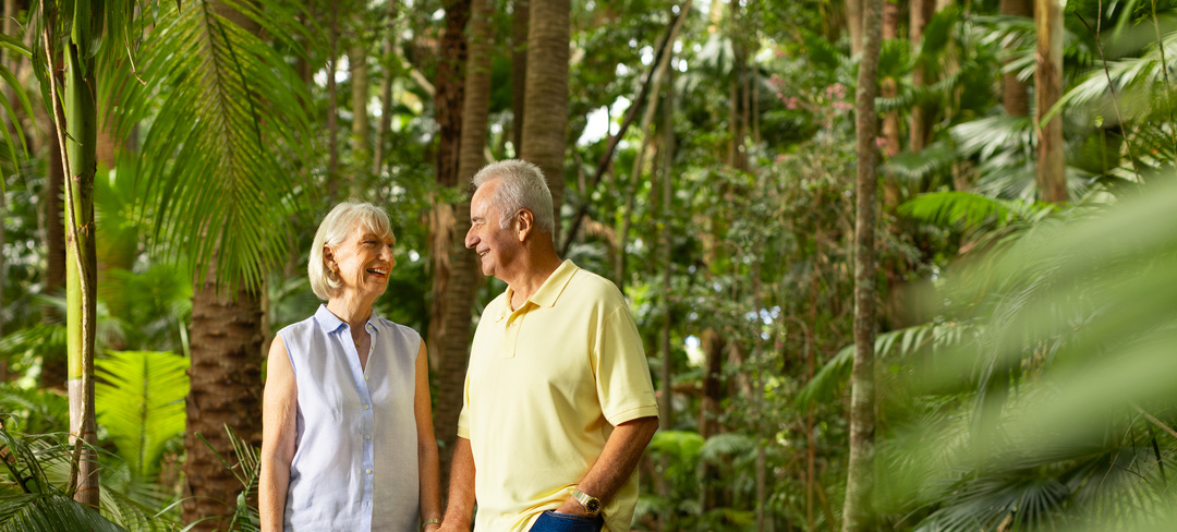 A retired couple holding hands in a lush forest