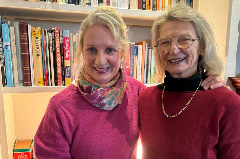 Mum and daughter standing in front of a home library in a room and smiling at the camera
