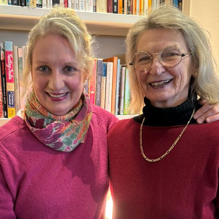 Mum and daughter standing in front of a home library in a room and smiling at the camera