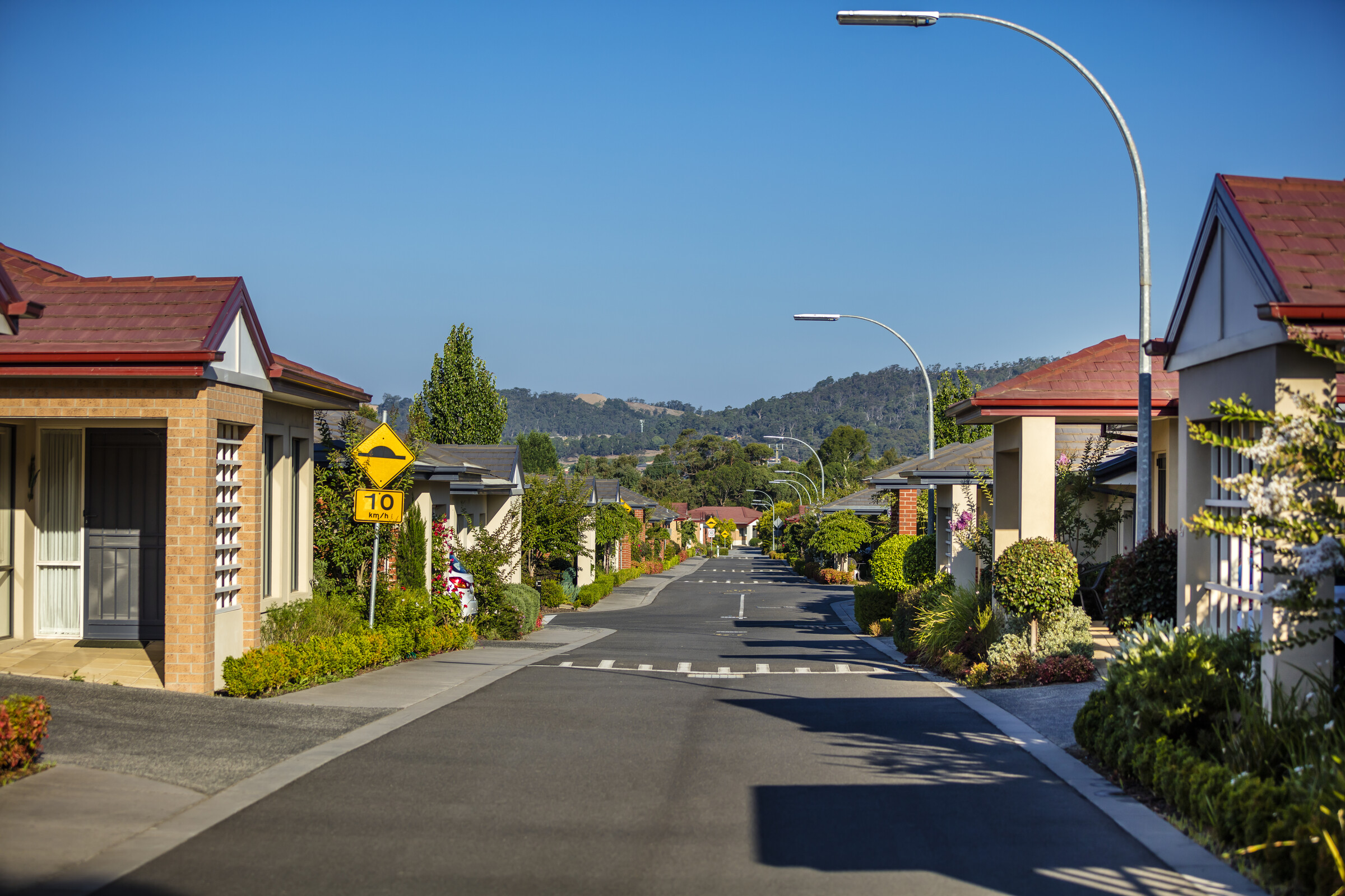 Waverley Country Club village roadway lined with homes, trees, gardens and lamp posts, hills in the distance
