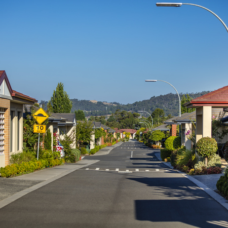 Waverley Country Club village roadway lined with homes, trees, gardens and lamp posts, hills in the distance