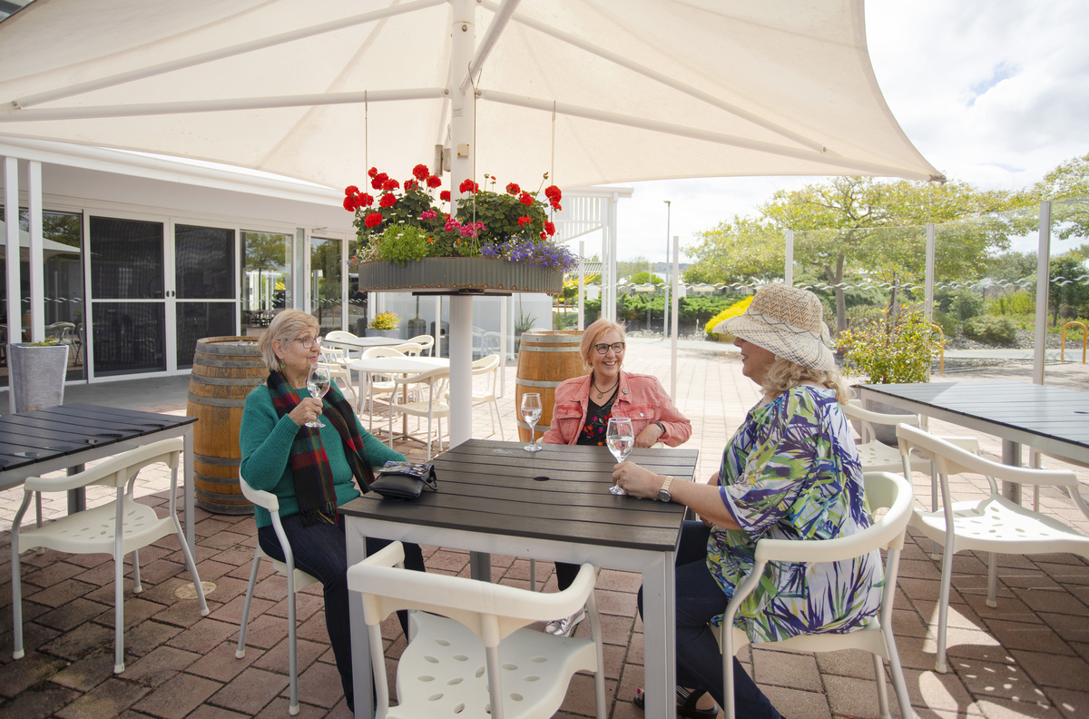 Three elderly women sitting under a shaded alfresco and chatting