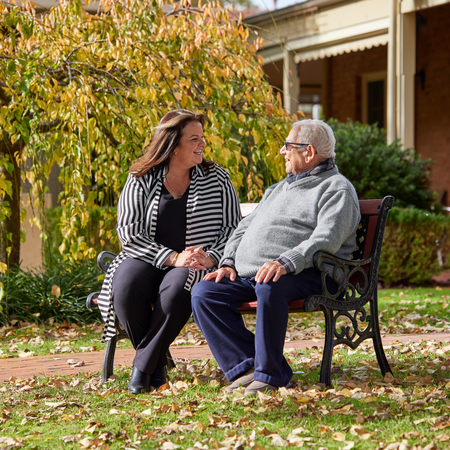 Retirement village manager Nicole sitting on a bench outside Fiddlers Green with an elderly resident