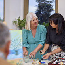 Two female retirement village residents smiling at each other while painting