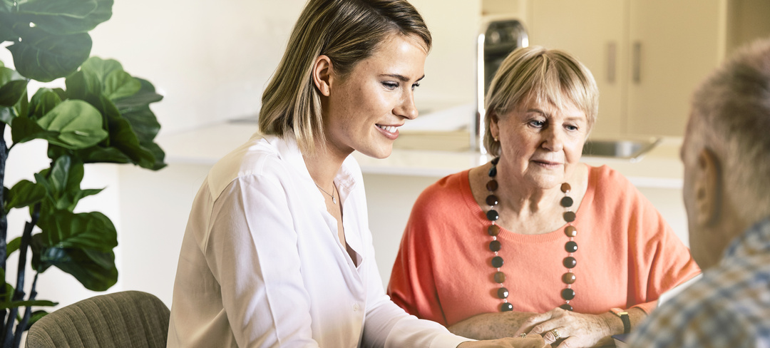 An elderly woman and man are sitting at a table next to their retirement financial adviser.