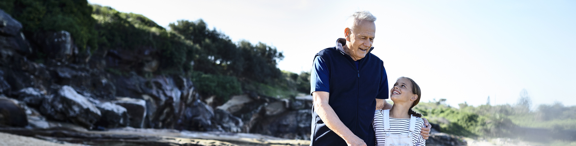 A grandpa walking on the beach with his granddaughter shows one of the many delights of being a grandparent.