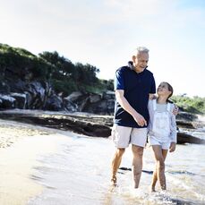A grandpa walking on the beach with his granddaughter shows one of the many delights of being a grandparent.