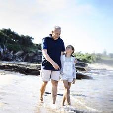 A grandpa walking on the beach with his granddaughter shows one of the many delights of being a grandparent.