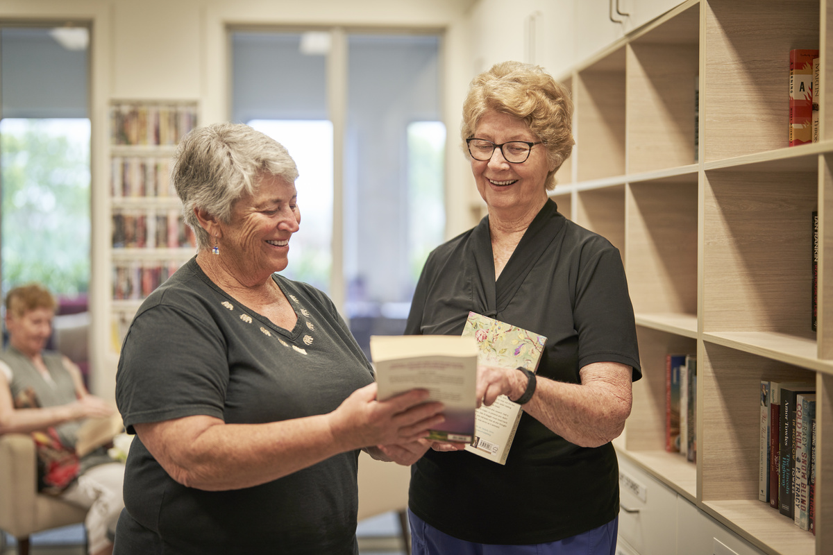 Two senior ladies looking at each other's book titles