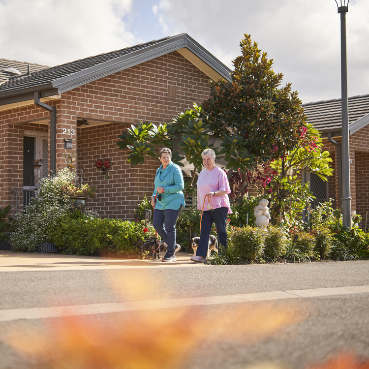 Two women walking their dogs past freestanding homes in their retirement village