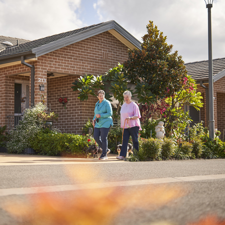 Two women walking their dogs past freestanding homes in their retirement village