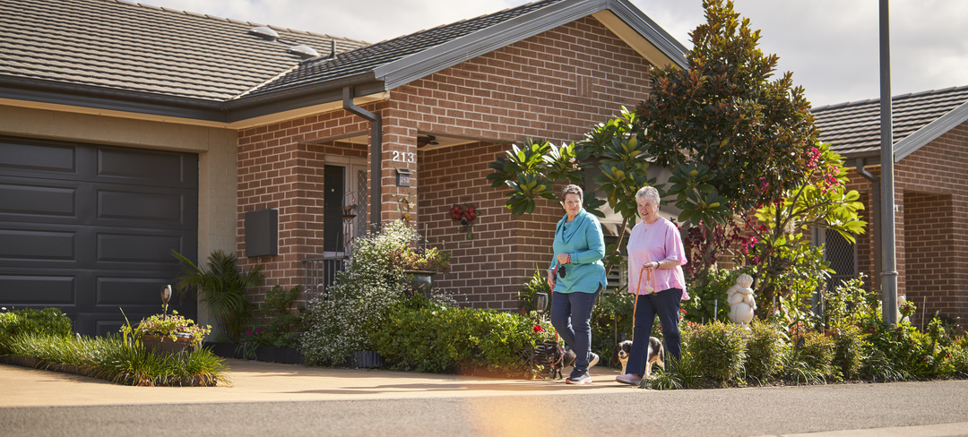 Two women walking their dogs past freestanding homes in their retirement village
