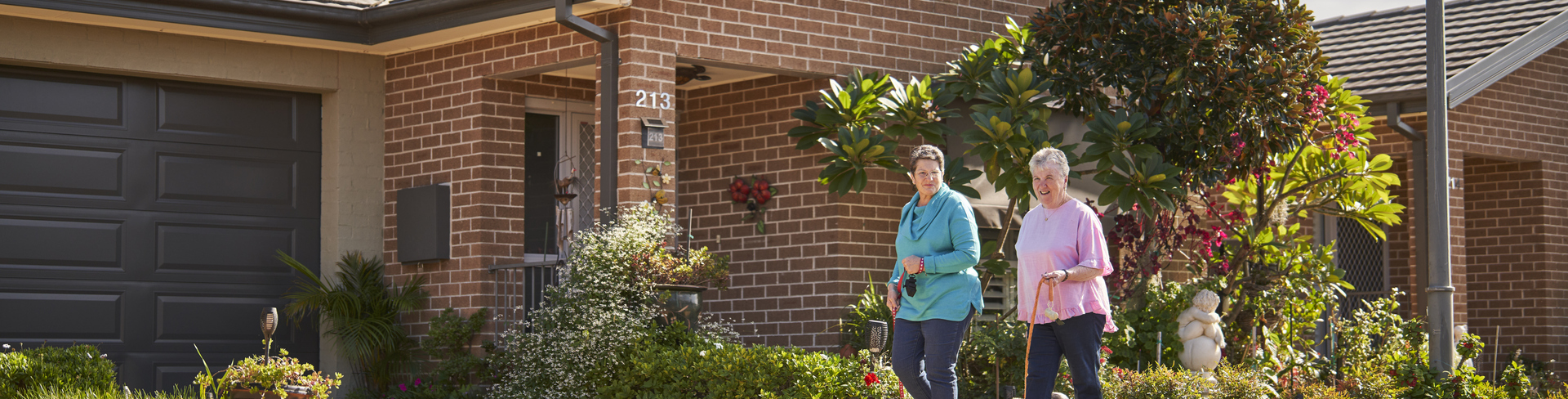 Two women walking their dogs past freestanding homes in their retirement village