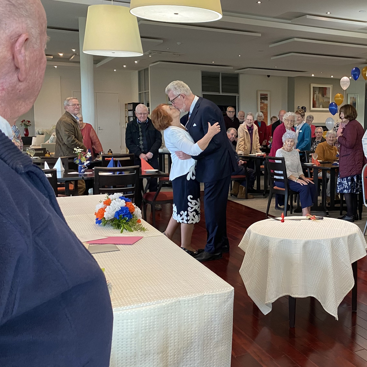 Pam and George kissing to a cheering crowd at their wedding reception in the Evelyn Ridge community centre