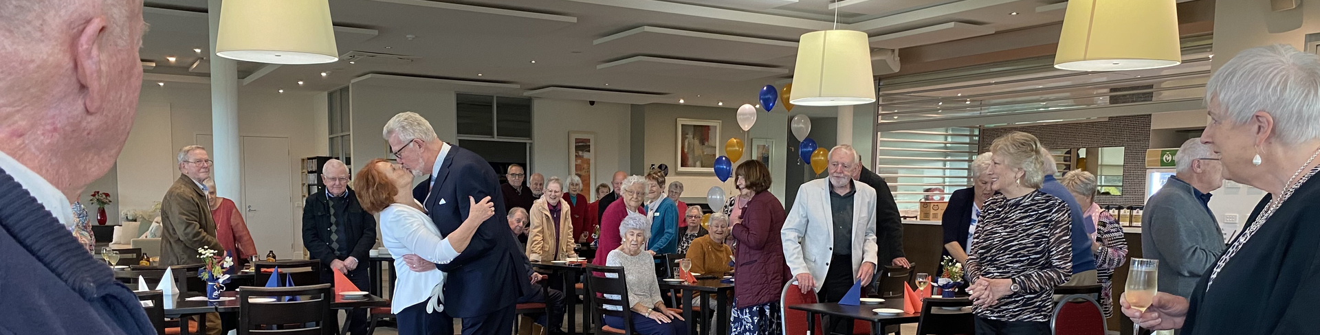 Pam and George kissing to a cheering crowd at their wedding reception in the Evelyn Ridge community centre