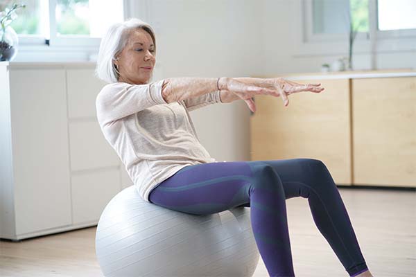 A senior lady sitting on a balance ball and leaning backwards as a form of exercise
