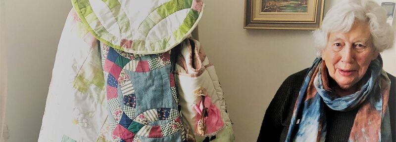 Retirement village resident Margaret stands next to a stunning patchwork quilt. 