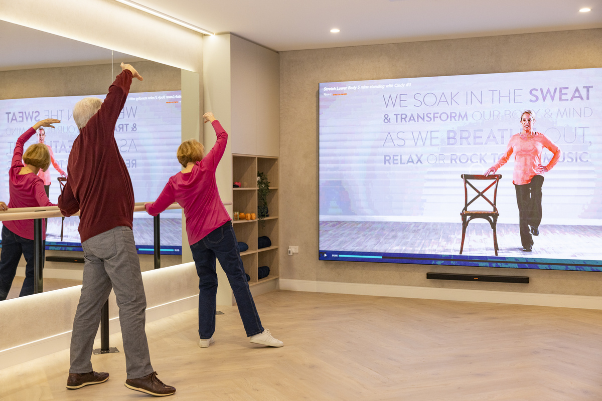 A couple exercising in the gym following instructions from a large screen