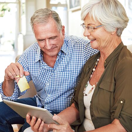 A man in a blue checked shirt sits next to his wife in a khaki shirt. She’s holding a tablet device, which has become a standard item for operating modern smart homes.