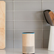 A cylinder timber Amazon Alexa Echo speaker sits on a kitchen bench.