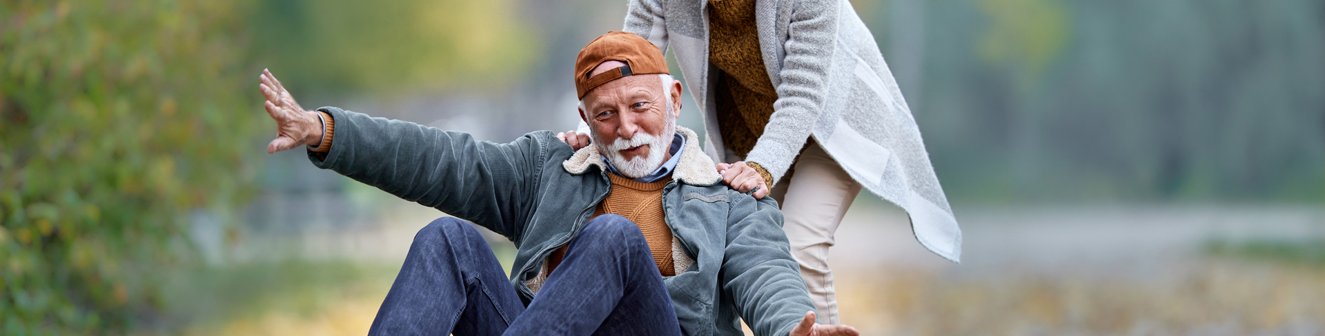 Woman pushing man sitting on a skateboard on wide cobblestone pathway