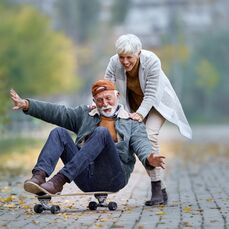 Woman pushing man sitting on a skateboard on wide cobblestone pathway